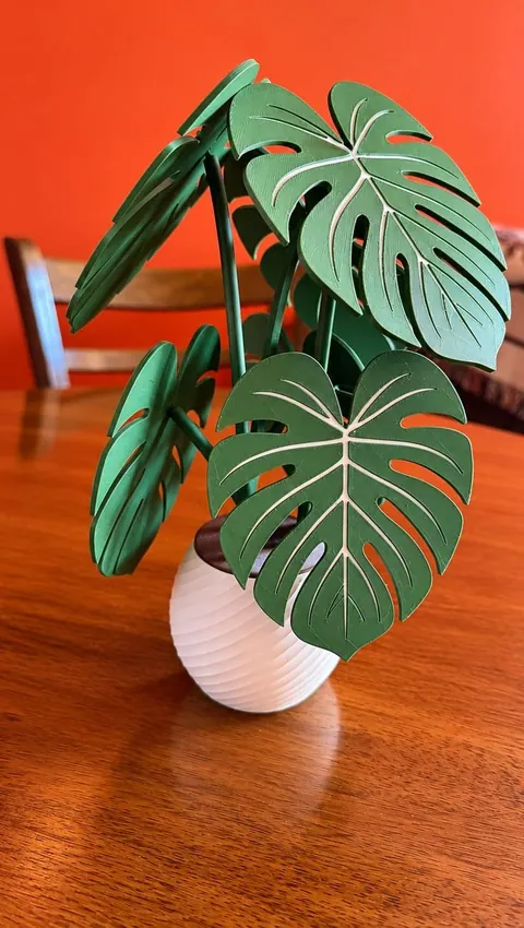 Planta Monstera impresa en 3D con hojas verdes y maceta blanca sobre una mesa de madera