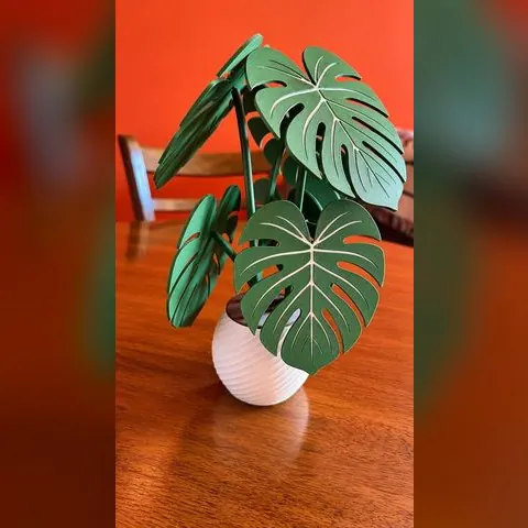 Planta Monstera impresa en 3D con hojas verdes y maceta blanca sobre una mesa de madera